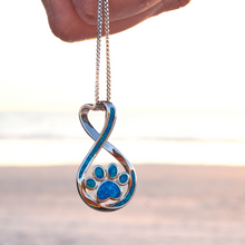 Load image into Gallery viewer, Opal Infinity Love Paw Necklace hanging close for a shot with a blurred beach background.