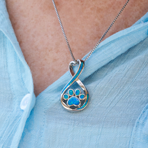 Opal Infinity Love Paw Necklace displayed closely by being worn around a woman's neck.
