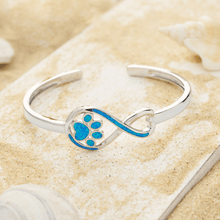 Load image into Gallery viewer, Opal Infinity Love Paw Cuff Bracelet displayed by being placed on top of a sand covered driftwood.