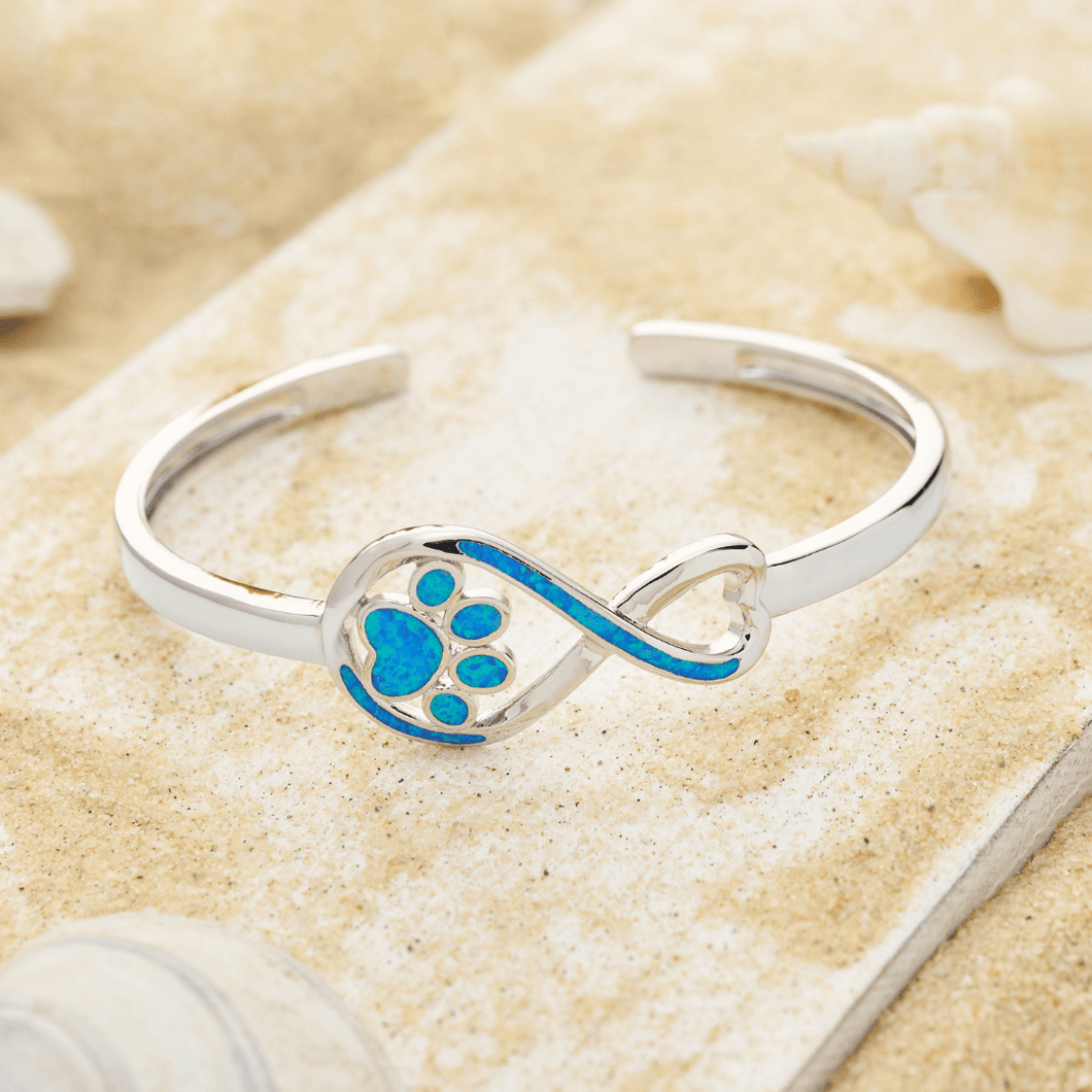 Opal Infinity Love Paw Cuff Bracelet displayed by being placed on top of a sand covered driftwood.