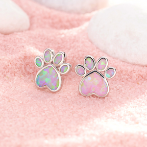 Opal Love Paw Studs in Pink are displayed on a pink sandy surface.