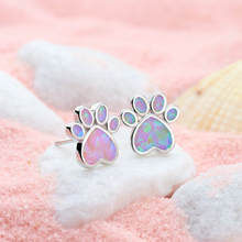 Load image into Gallery viewer, Opal Love Paw Studs in Pink resting on a white stone in a pink sandy environment.