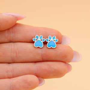 Opal Love Paw Studs are displayed by placing them on a woman's palm, nestled between her two fingers.