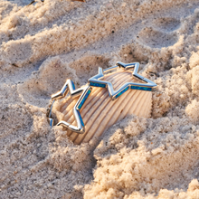 Load image into Gallery viewer, Opal Star Hoop Earrings resting on a shell partially buried in the sand.