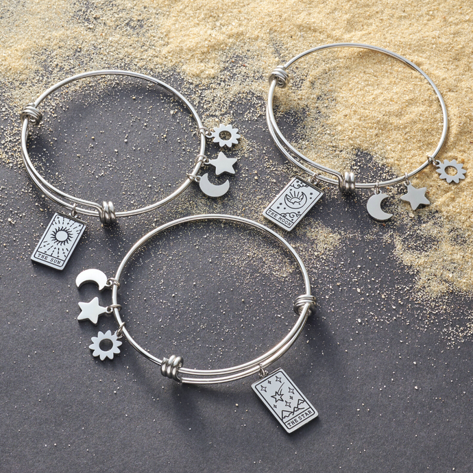 Bracelets featuring Moon Tarot, Sun Tarot, and Star Tarot Cards displayed on a gray surface with sandy grains.