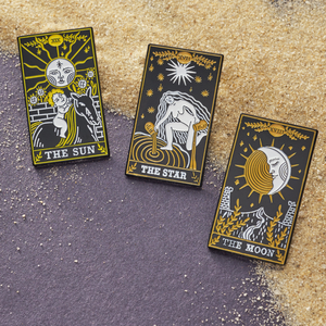 Moon Tarot, Sun Tarot, and Star Tarot Card Pins are placed on sandy grains.