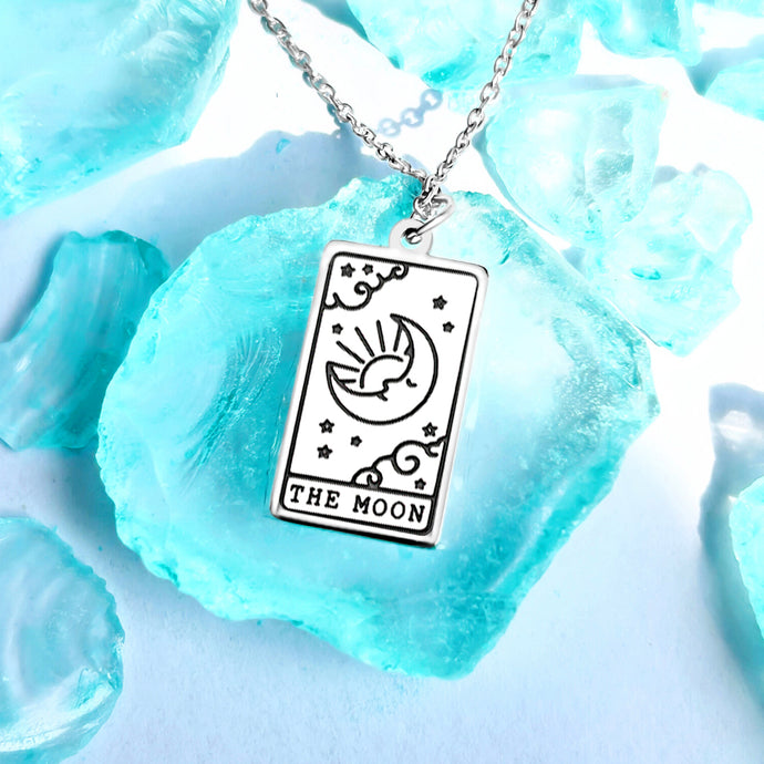 The Moon Tarot Card Necklace displayed on a blue crystal surrounded by other blue crystals.