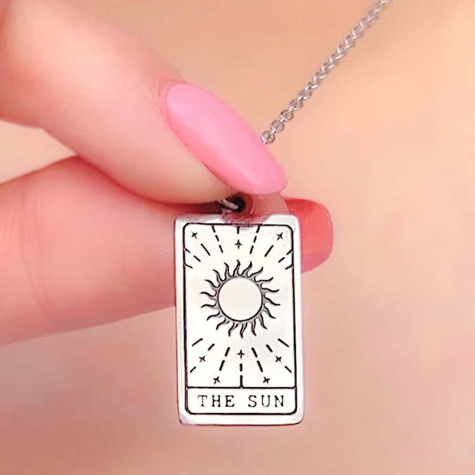 The Sun Tarot Card Necklace displayed closely by being held by a woman's finger.