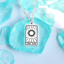 Load image into Gallery viewer, The Sun Tarot Card Necklace displayed on a blue crystal surrounded by other blue crystals.
