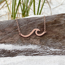 Load image into Gallery viewer, The Wave Necklace is displayed by hanging it on a piece of driftwood with sand below.