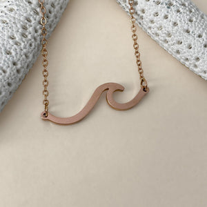 The Wave Necklace is displayed on a smooth, dirty white surface.
