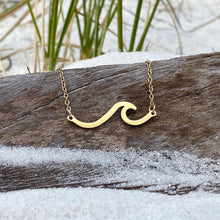 Load image into Gallery viewer, The Wave Necklace is displayed by hanging it on a piece of driftwood with sand below.