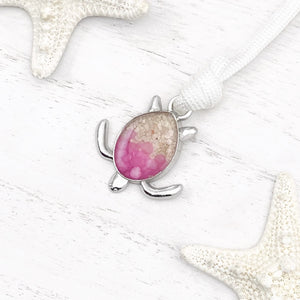 White Rope Sand Sea Turtle Bracelet in Pink Pebble is displayed on a white wooden surface.