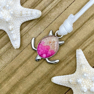 White Rope Sand Sea Turtle Bracelet in Pink Pebble is displayed on a wooden surface.